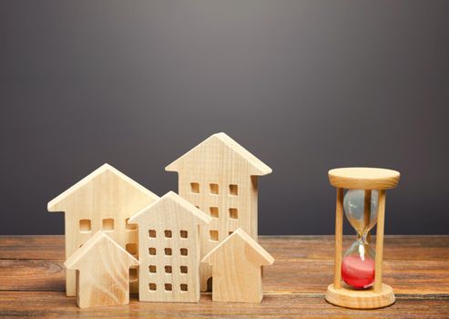 Wooden figures of houses and sand hourglass. Mortgage and loan concept. Temporary rental housing and residence permit. Time to pay taxes and bills. Realtor services for a quick search for options.