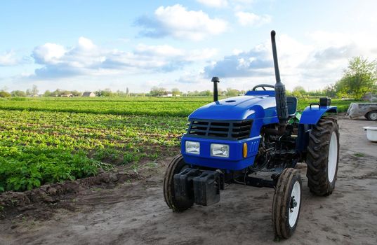 Blue tractor without driver near a farm field. Agricultural machinery and technology. Organization of agricultural activities, business planning. Support for farmers with subsidies and loans.