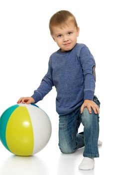 Beautiful little boy in jeans and a blue shirt. The boy stands on the knee and holds a hand ball - Isolated on white background