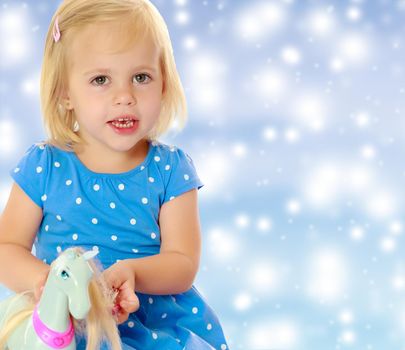 Cute little blonde girl playing with a toy horse. Girl wearing a blue dress with polka dots.On a blue background with large, white, Christmas or new year's snowflakes.