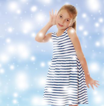 Caucasian little girl in a striped summer dress, listening. Girl holding a hand to his ear.On a blue background with large, white, Christmas or new year's snowflakes.