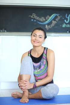 Portrait of smiling yoga woman sitting at yoga mat after workout at yoga studio. Yoga. Woman