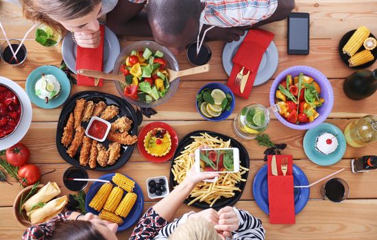 Top view of group of people having dinner together while sitting at wooden table. Food on the table. People eat fast food