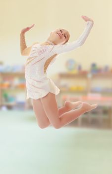 Beautiful little girl gymnast dressed in sports swimsuit, jumps high.On the background of the room where children live, and are on the shelves of toys.