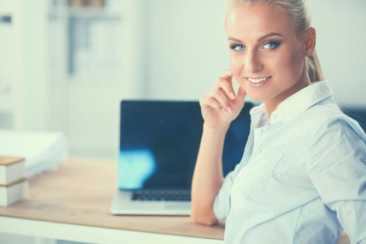 Attractive businesswoman sitting on a desk with laptop in the office.