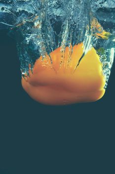 Fresh yellow paprika splash in water on black background.