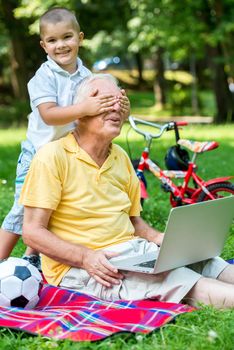 happy elderly senior grandfather and child in park using laptop computer