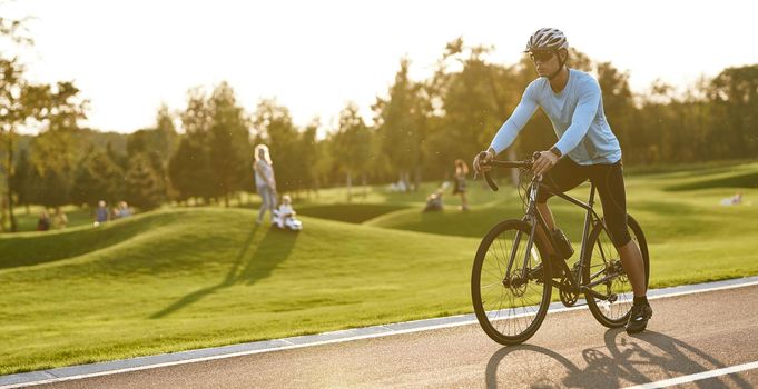 Professional road bicycle racer training outdoors. Young athletic man in sportswear and protective helmet standing with bicycle on the road in park, getting ready to ride. Active lifestyle and sport