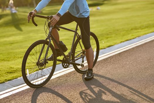 Cycling at sunset. Cropped shot of a man in sportswear standing with his bicycle on the road in park on a summer day. Active lifestyle and sport