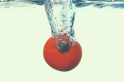 Fesh tomato splashing out of water on white background.
