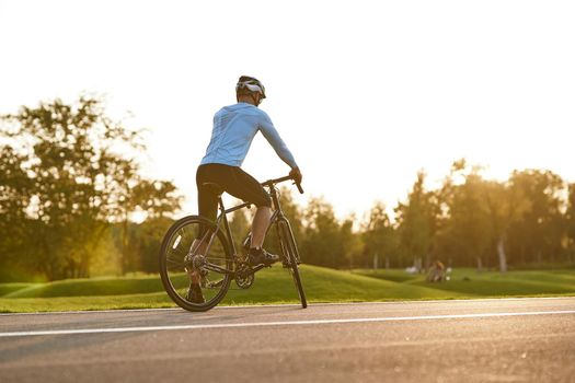 Ready to ride. Rear view of athletic man in sportswear cycling outdoors at sunset, professional racer standing with bicycle on the road and enjoying amazing nature view. Active lifestyle and sport