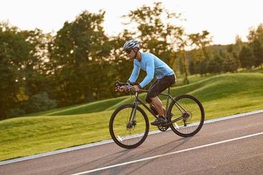 Side view of a young athletic man in sportswear, professional bicycle racer riding mountain road bike in the city park at sunset. Healthy active lifestyle and sport concept