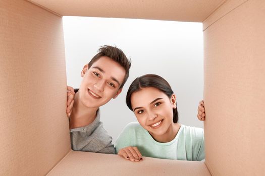 Cheerful teen couple unpacking, opening carton box and looking inside with a smile on their faces. They are delighted with the speed of delivery of goods.