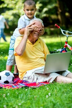 happy elderly senior grandfather and child in park using laptop computer