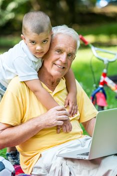 happy elderly senior grandfather and child in park using laptop computer