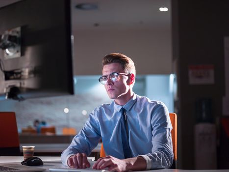 Young man working on computer at night in dark office. The designer works in the later time.