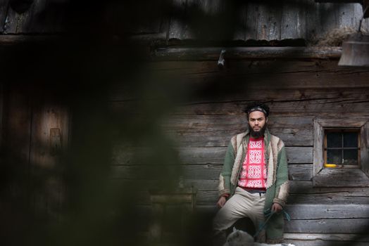 handsome young hipster man standing together with white husky dog in front of old vintage retro wooden house