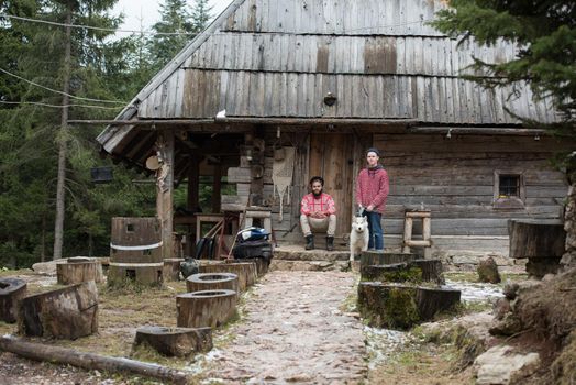 hipsters couple portrait, two young  man with white husky dog  sitting in front of old wooden retro house