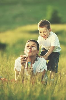 happy child and woman outdoor playing with soap bubble on meadow