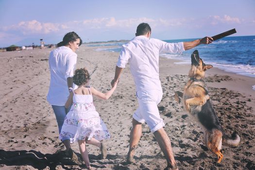 happy young family in white clothing have fun and play with beautiful dog at vacations on beautiful beach 