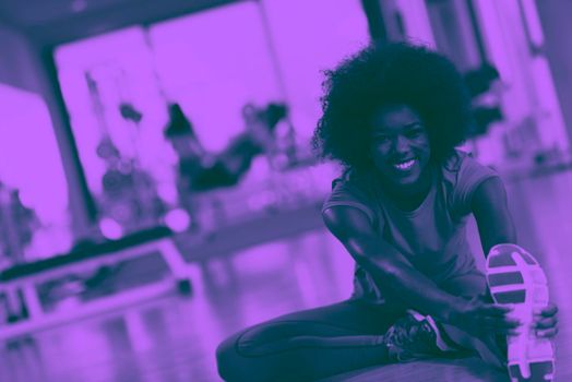 happy young african american woman in a gym stretching and warming up before workout young mab exercising with dumbbells in background duo tone filter