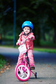 Cute smiling little girl with bicycle and helmet on road in the park