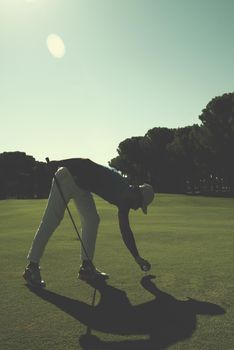 golf player placing ball on tee. beautiful sunrise on golf course landscape  in background