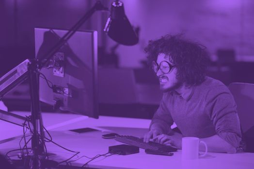 Young man working on computer at night in dark startup office. The designer works in the later time. duo tone