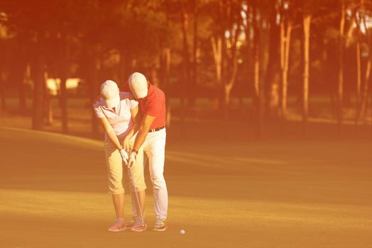 male golf instructor teaching female golf player, personal trainer giving lesson on golf course