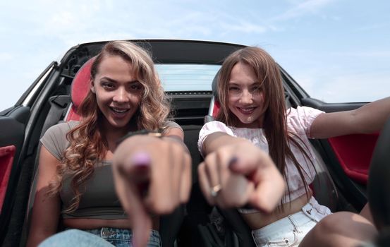 two happy girlfriends sitting in a car and pointing at you.the concept of choice