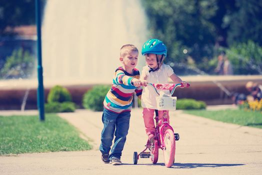 Happy childrens outdoor,  brother and sister in park have fun. Boy and girl in park learning to ride a bike.