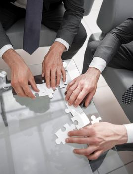 close up.business people putting together a puzzle ,sitting behind a Desk.the concept of cooperation