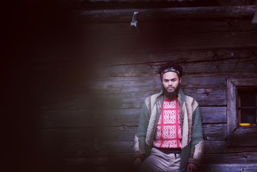 portrait of young hipster,  man with beard in front of old vintage wooden house