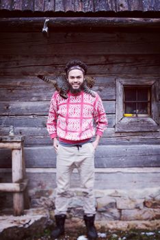 portrait of young hipster man with beard and cat in front of wooden house