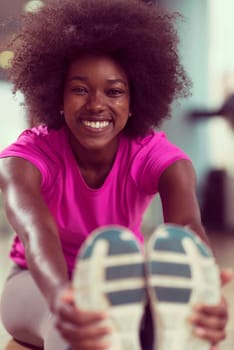 happy young african american woman in a gym stretching and warming up before workout