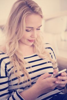 young happy woman sitting on sofa with mobile phone at luxury home