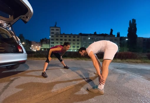 jogging couple warming up and stretching before evening running in the city