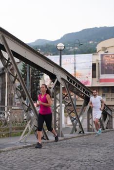 urban sports, healthy young couple jogging across the bridge in the city at sunny morning