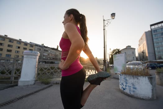 athlete woman warming up and stretching while preparing for running on the city street at  sunny morning