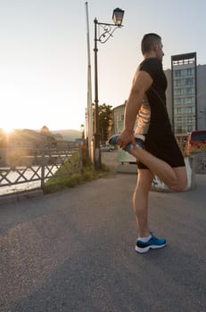 athlete man warming up and stretching while preparing for running on the city street at  sunny morning