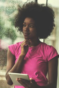 beautiful african american woman using tablet computer from home while rain and bad weather is outdoor