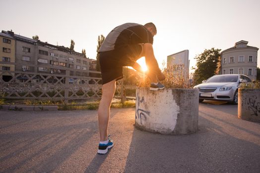 man tying running shoes laces getting ready to run on city at sunny morning