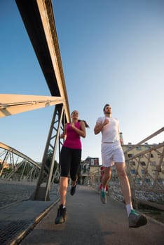 urban sports, healthy young couple jogging across the bridge in the city at sunny morning