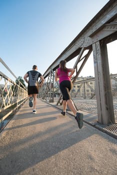 urban sports, healthy young couple jogging across the bridge in the city at sunny morning