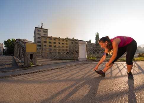 athlete woman warming up and stretching while preparing for running on the city street at  sunny morning