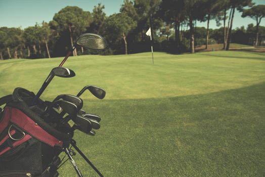 close up of golf bag on course with  club and ball in front at beautiful sunrise