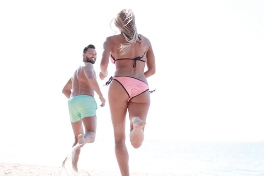 Happy couple running together among a beach at sunny day