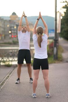 jogging couple warming up and stretching before morning running in the city