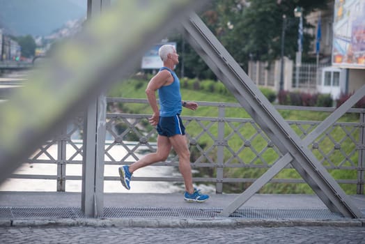 handsome senior man athlete jogging and  have morning workout with sunrise and city in background