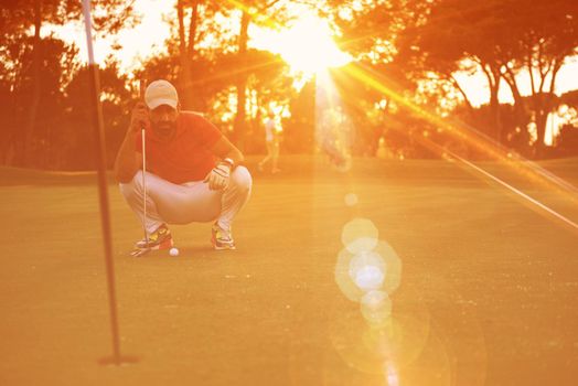 golf player aiming shot with club on course at beautiful sunset with sun flare in background